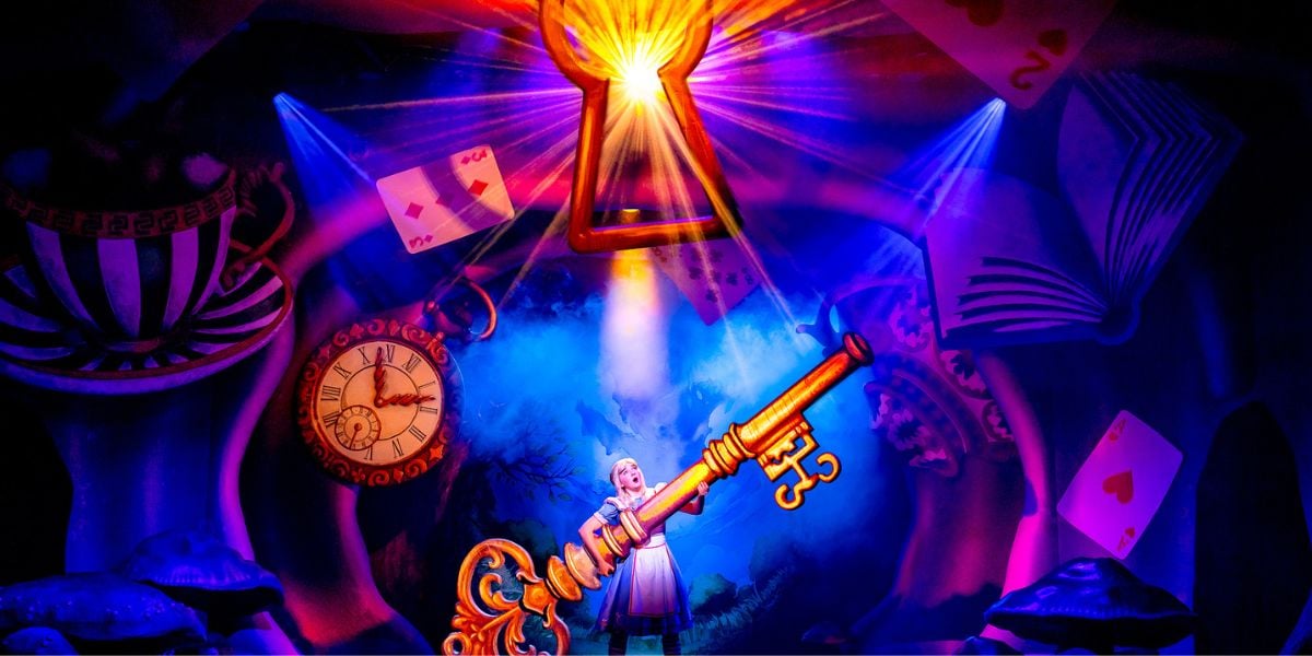 Alice in Wonderland at Riverside Studios. Alice (Charlotte Bradley) holds an oversized key and a large keyhole hangs glowing overhead.