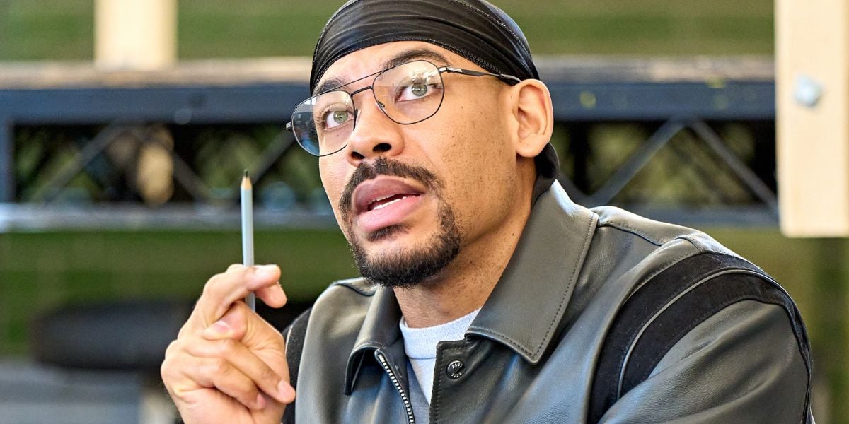 Aaron Pierre wearing glasses, a durag and a black leather jacket with a fake cigarette in his hand rehearsing for One Flew Over the Cuckoo's Nest at the Old Vic.