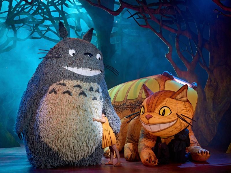 My Neighbour Totoro production photo with two large puppets and an actor hugging Totoro.