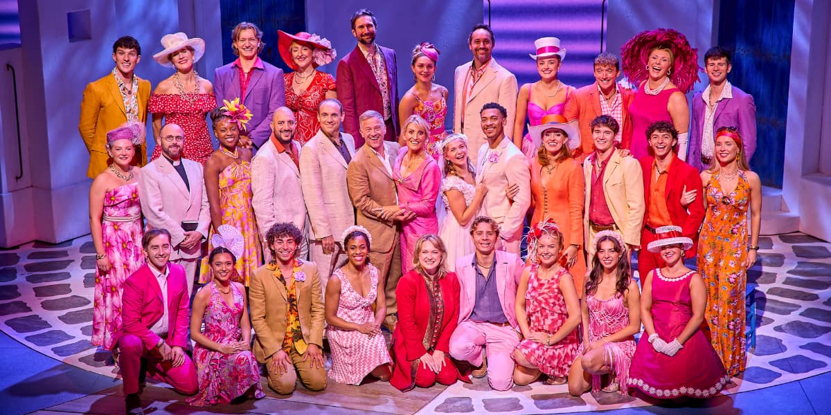 The cast of MAMMA MIA! are dressed in pink and orange wedding outfits