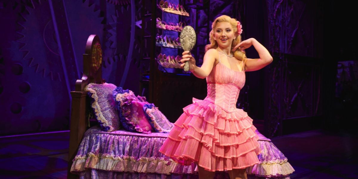 Zizi Strallen as Glinda in Wicked, London. Wearing a pink dress checking her hair in a mirror.