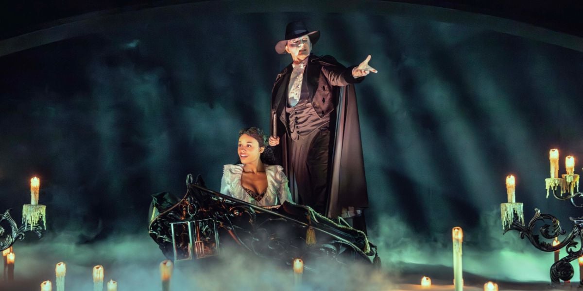 Phantom of the Opera production shot with Dean Chisnall and Beatrice Penny-Touré. They are on a boat surrounded by smoke and candles.
