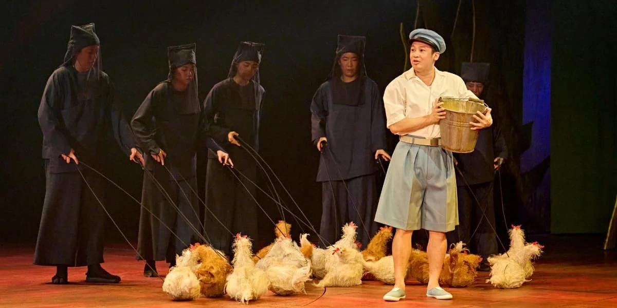 Kanta, a boy in a blue cap, holds a bucket surrounded by charming chicken puppets in My Neighbour Totoro, the multi-award-winning stage show now confirmed to close in London on 10 January 2027.