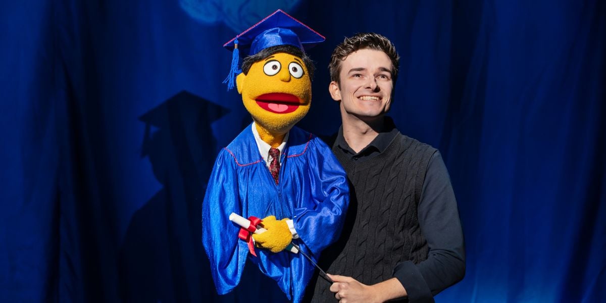 Noah Harrison in Avenue Q. The puppet wears a blue cap and gown with a diploma in hand. Photo by Matt Crockett