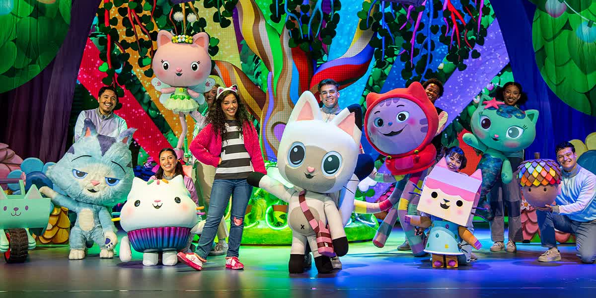 Gabby's Dollhouse Live! The main character Gabby is surrounded by performers with large puppet cats stood in front of a large rainbow backdrop.