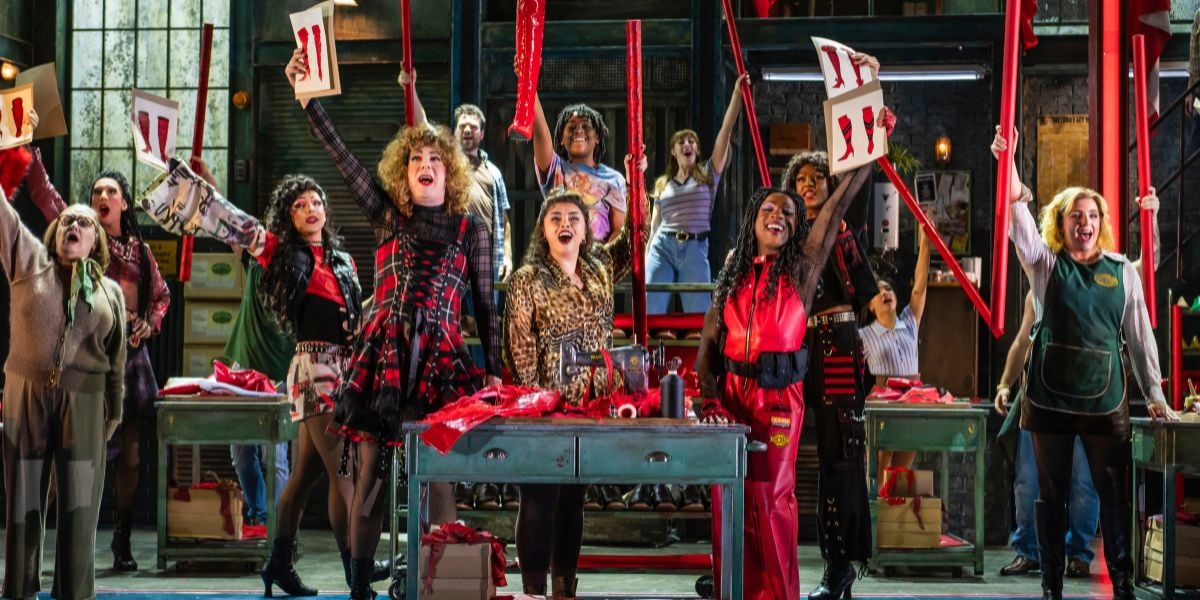 The company of Kinky Boots, holding red heeled boots to the air.