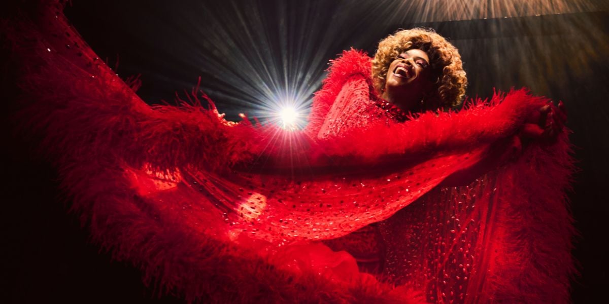 Johannes Radebe as Lola in Kinky Boots wearing an extravagant red dress.