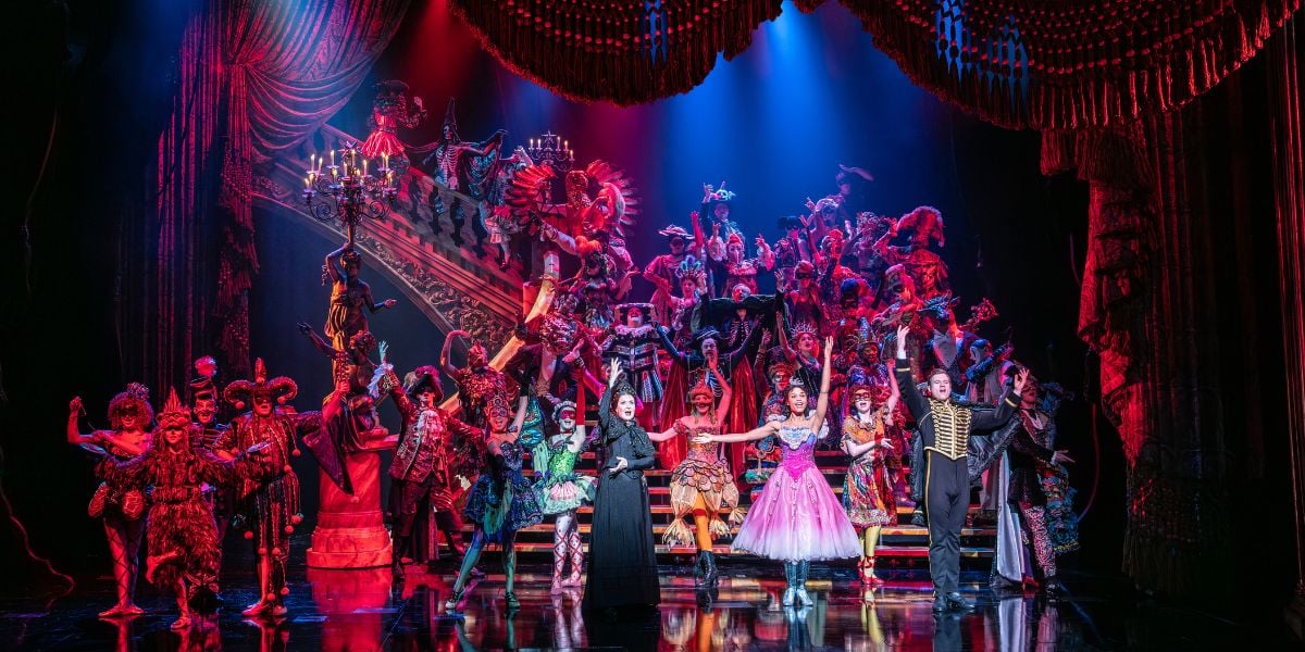 Phantom of the Opera company during Masquerade on a grand staircase in lavish costumes.