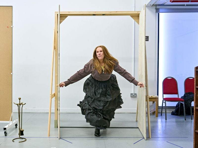 Catherine Tate in rehearsals for Oh, Mary! She wears a black frilled skirt and is bursting through a door.