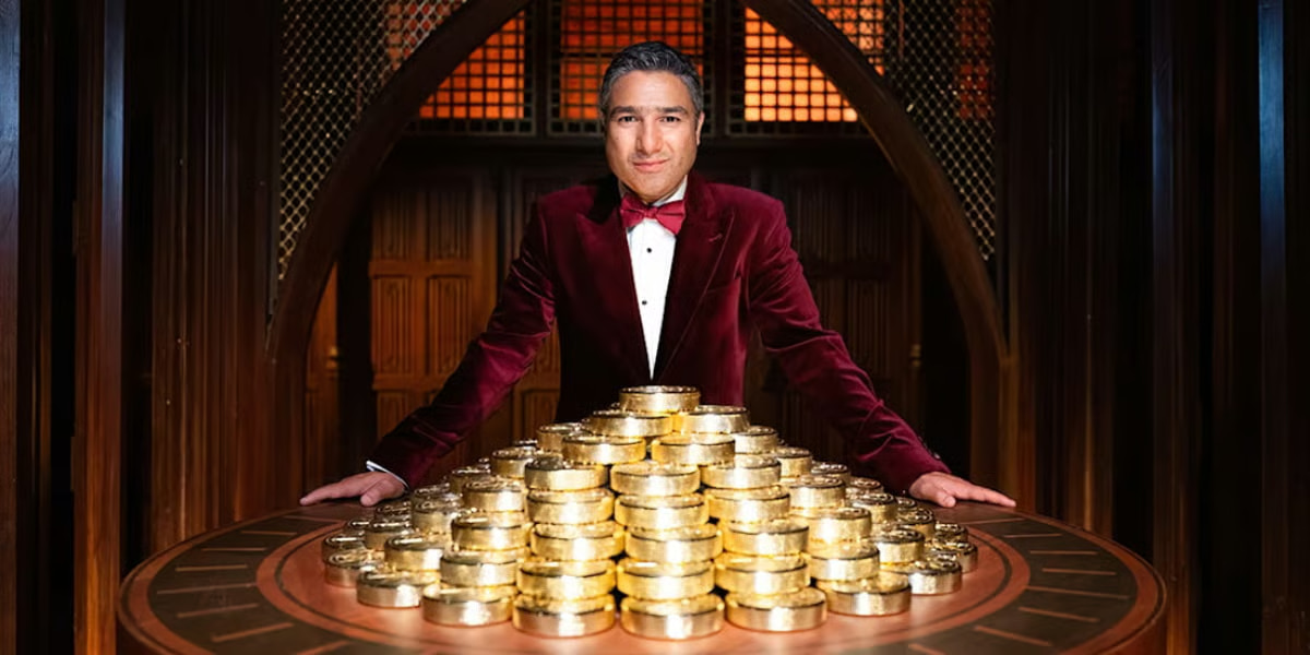 Nick Mohammed as the host in The Traitors – Acts of Betrayal London play, standing in front of a pile of gold.