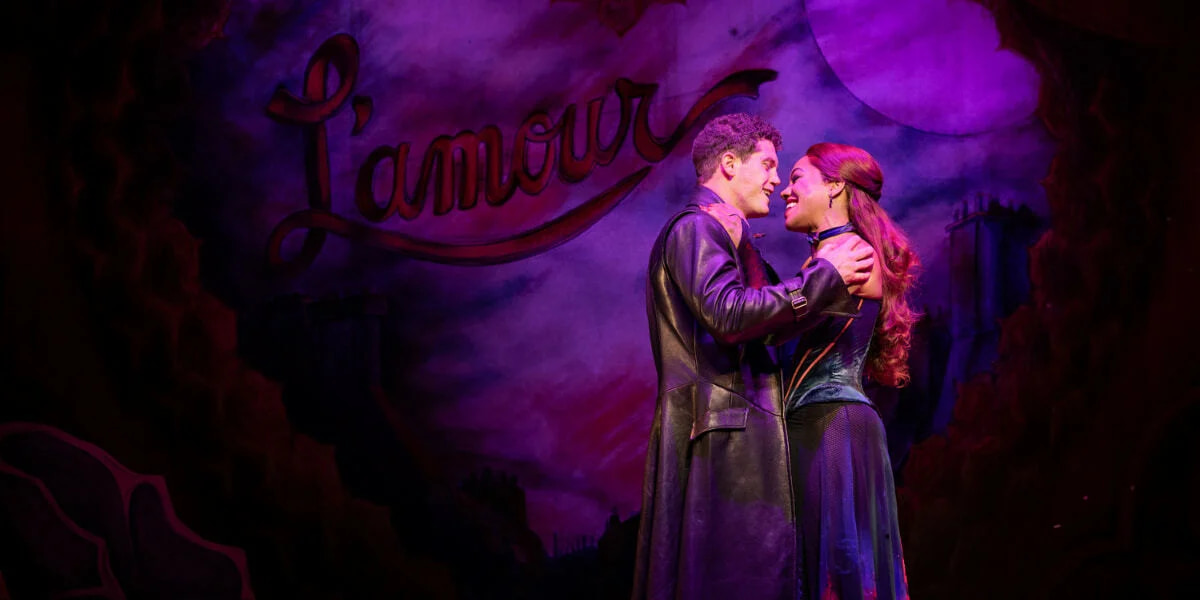 Satine, played by Karis Anderson, and Christian embrace beneath purple lighting in a romantic moment from Moulin Rouge! The Musical London.