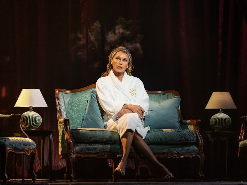 Vanessa Williams as Miranda Priestly in The Devil Wears Prada Musical in London. She wears a white robe and a headband, looking natural on the sofa.