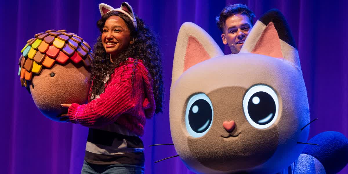 Gabby wearing cat ears holds a large acorn, stood next to another performer with a large cat puppet.