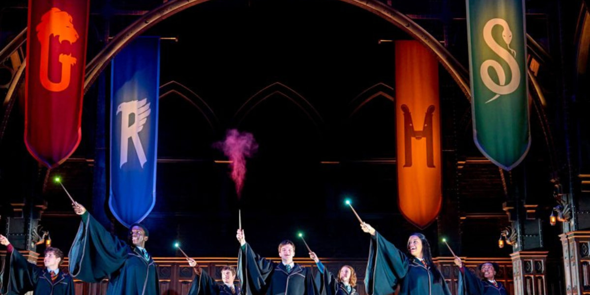 Members of the Harry Potter and the Cursed Child cast stand beneath their house banners, holding their wands aloft.