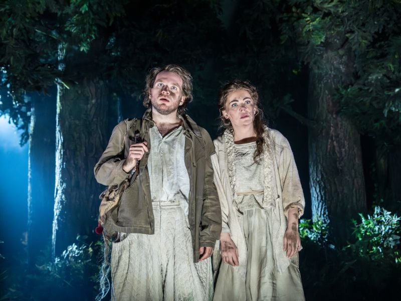 Into The Woods production shot at the Bridge Theatre. From left to right: Rachel Tucker (Baker’s Wife), and Hughie O’Donnell (the Baker) stood beside each other looking stunned. 