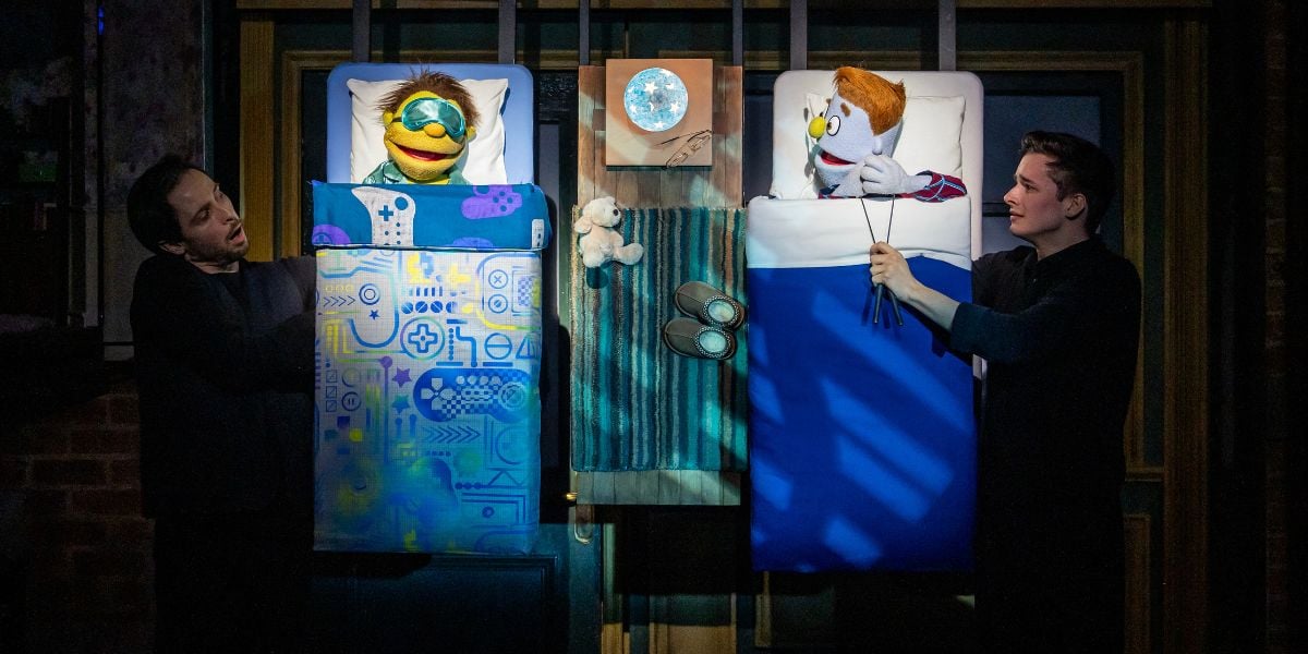 Charlie McCullagh and Noah Harrison in Avenue Q. Two puppets lie in bed, one wearing a eye mask and the other trying to get the other's attention. Photo by Matt Crockett