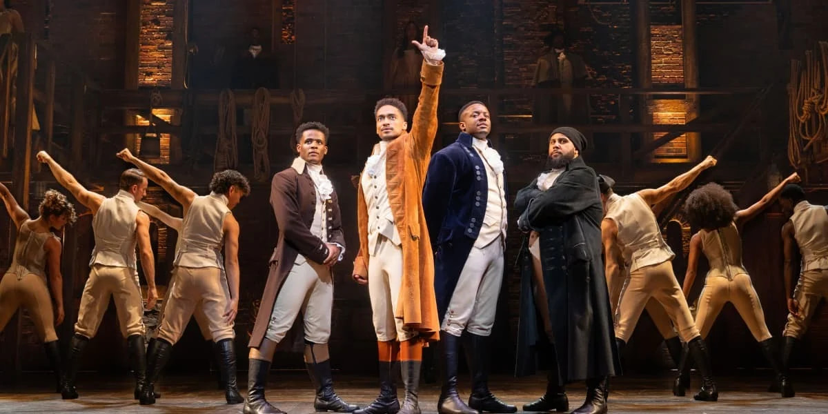 Cast performing on stage in Hamilton the musical, featuring Alexander Hamilton and ensemble in a high-energy scene