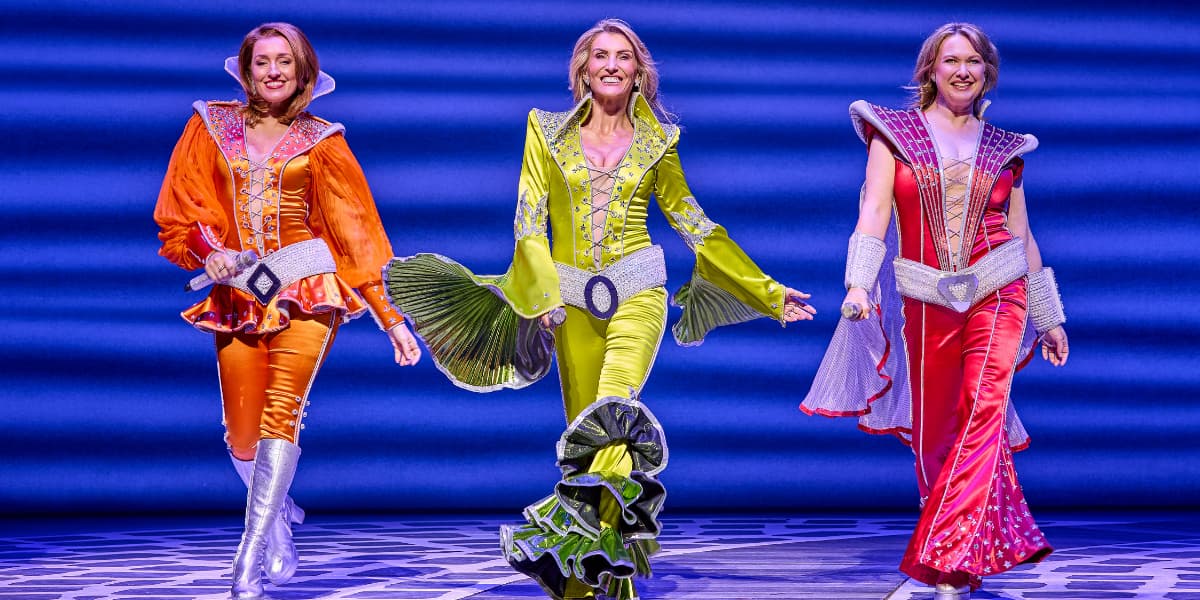Donna and the Dynamo's each wear a brightly coloured flared jumpsuit whilst dancing